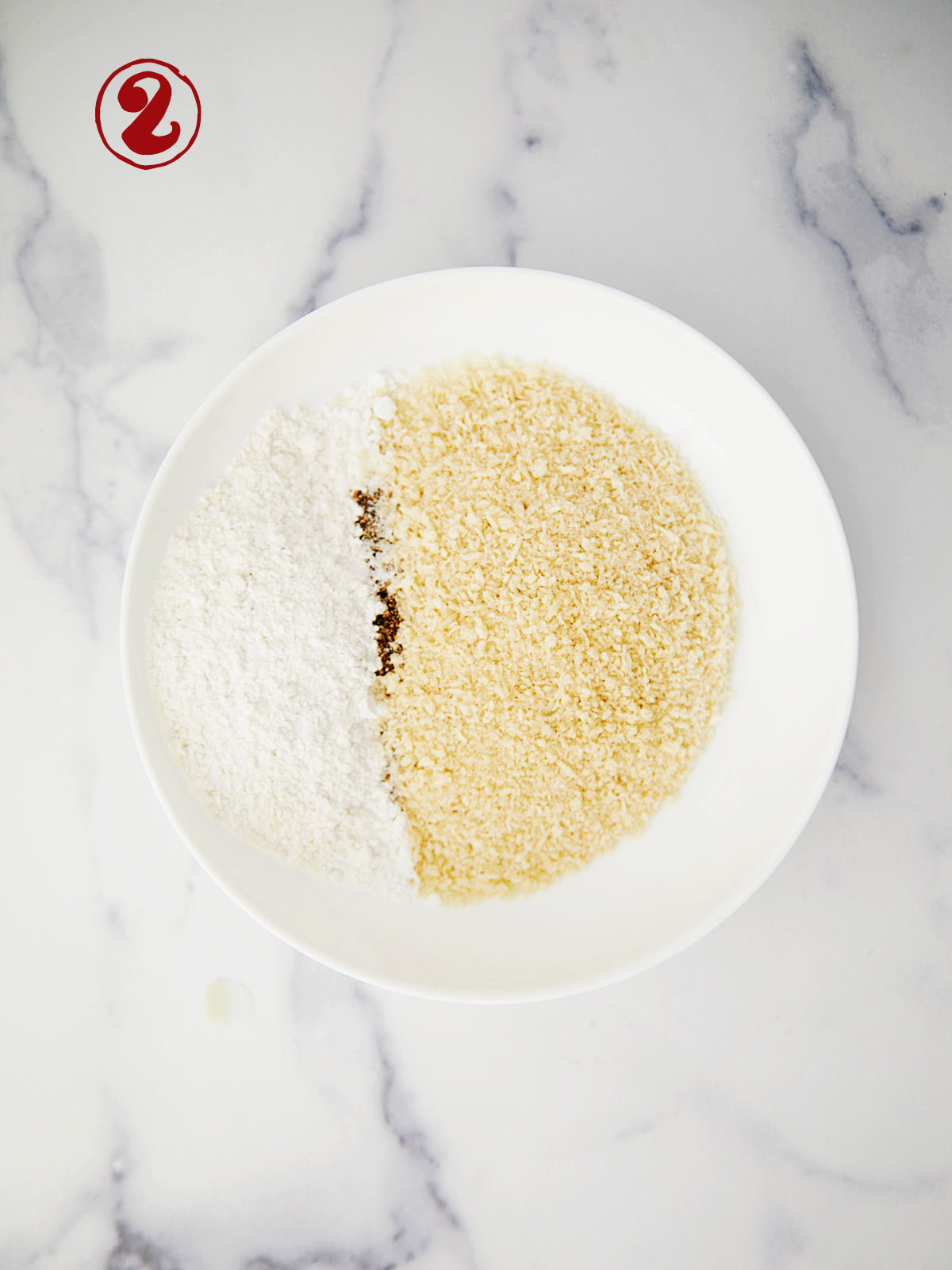 A white bowl with flour, breadcrumbs and salt and pepper.