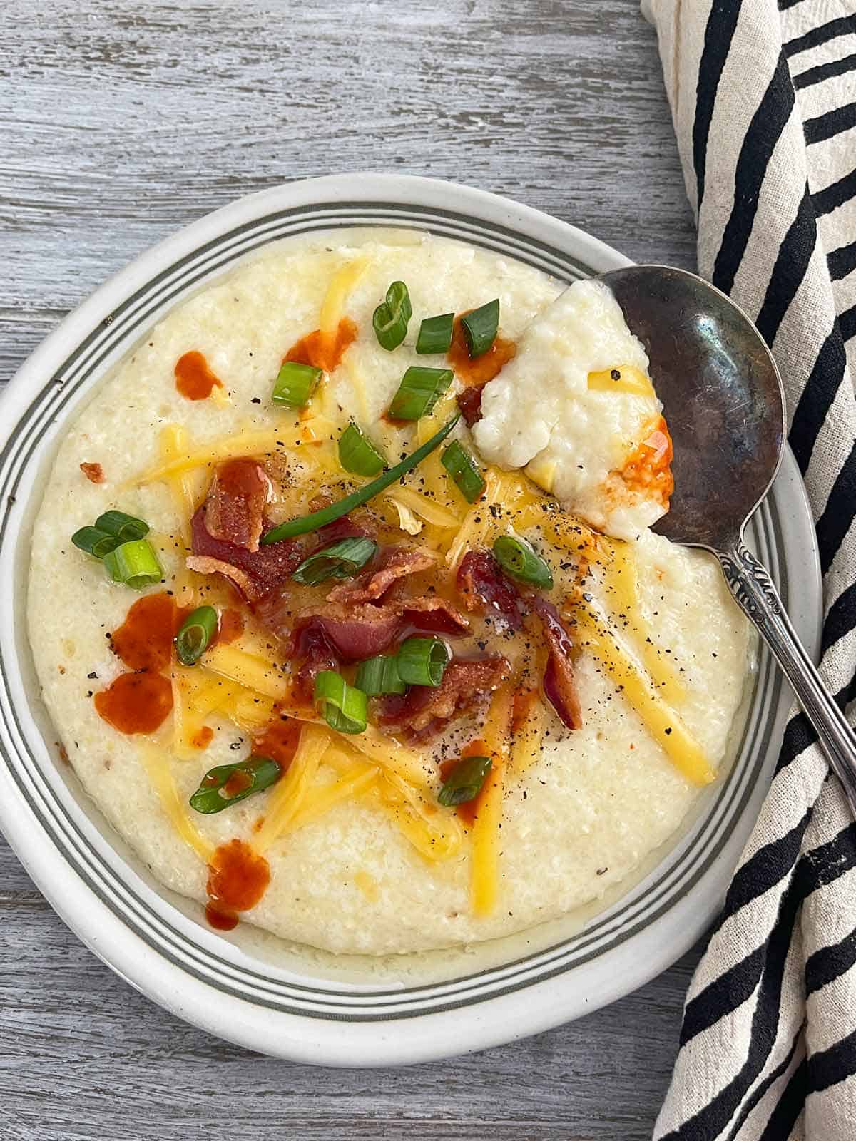 Grits on serving plate with melting butter, cheddar cheese, scallions, and bacon garnish.