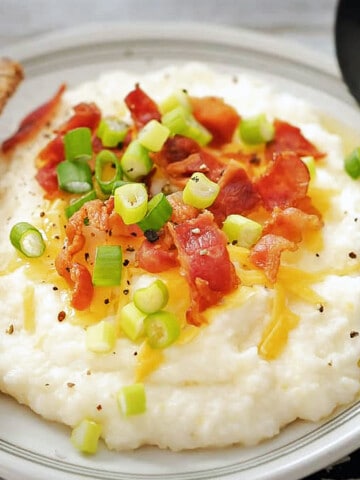 Plate of grits with bacon, scallions, and butter dripping down from the top.