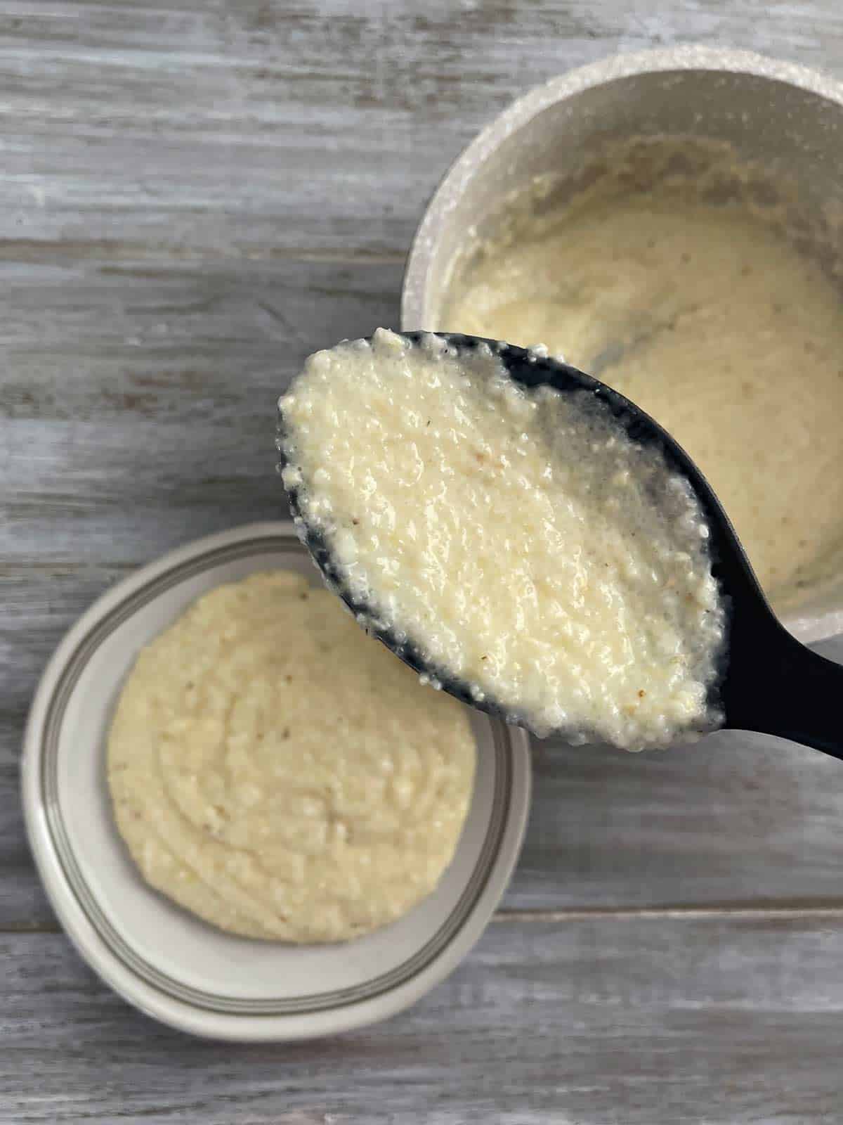 Cooked grits being spooned onto a serving plate.