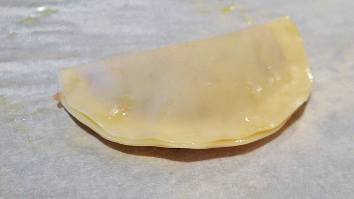 Folded Asian-style potsticker dough is sitting on top of a piece of paper.
