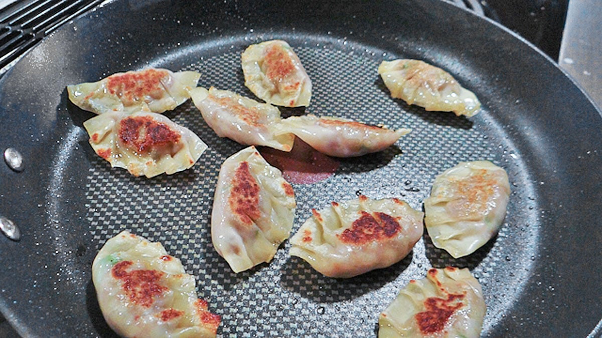 An Asian style frying pan with dumplings in it.