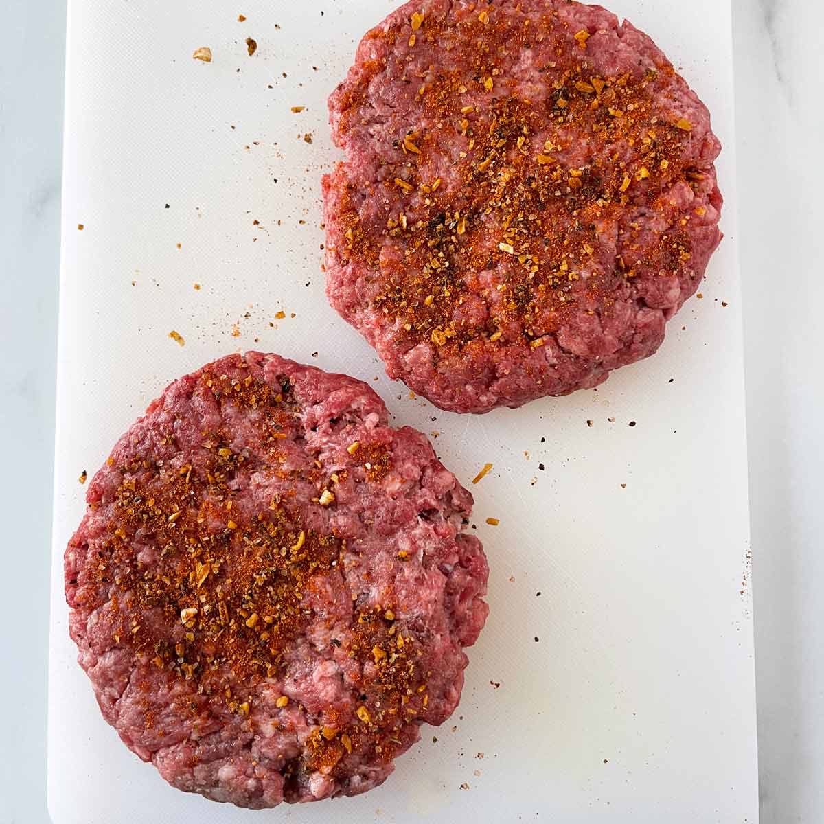 Two hamburger patties with seasoning.