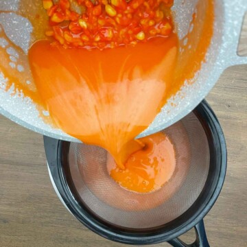Pouring melted candy corn and cream mixture through sieve into bowl.
