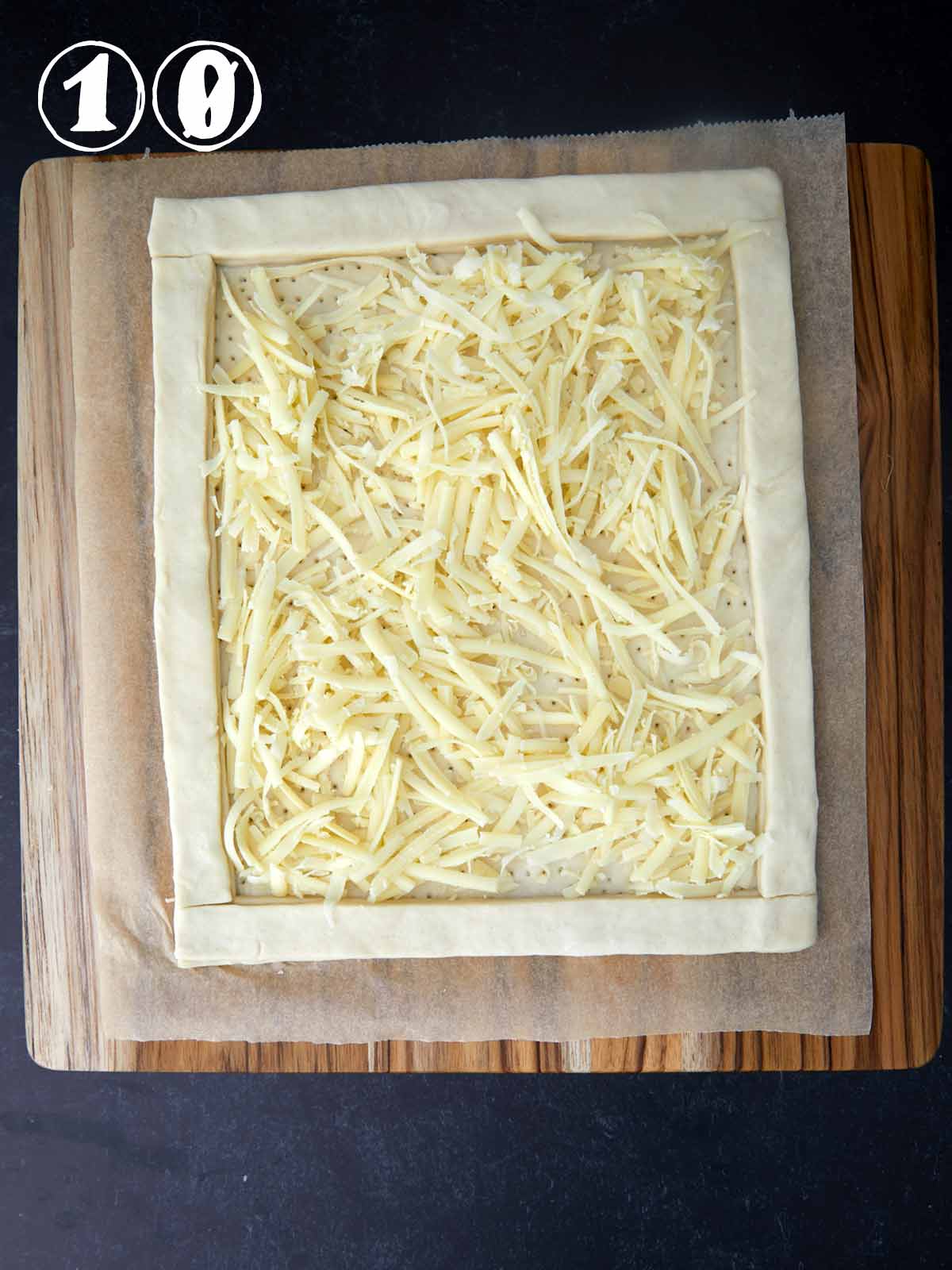 A square of GREEN tomato tart with Gruyère cheese atop puff pastry, placed on a cutting board.
