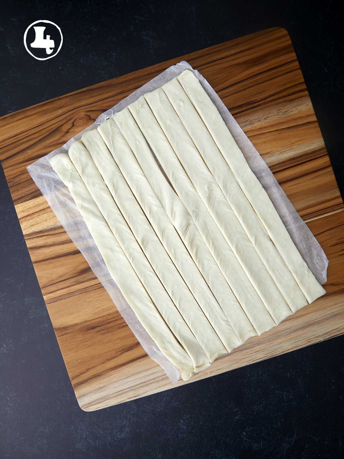 Puff pastry cut into narrow strips on a wooden cutting board.