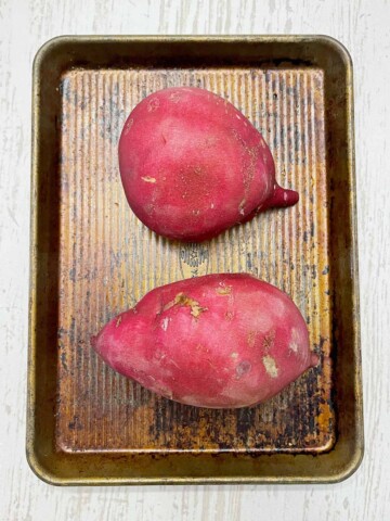 Two large garnet red sweet potatoes on a baking sheet.