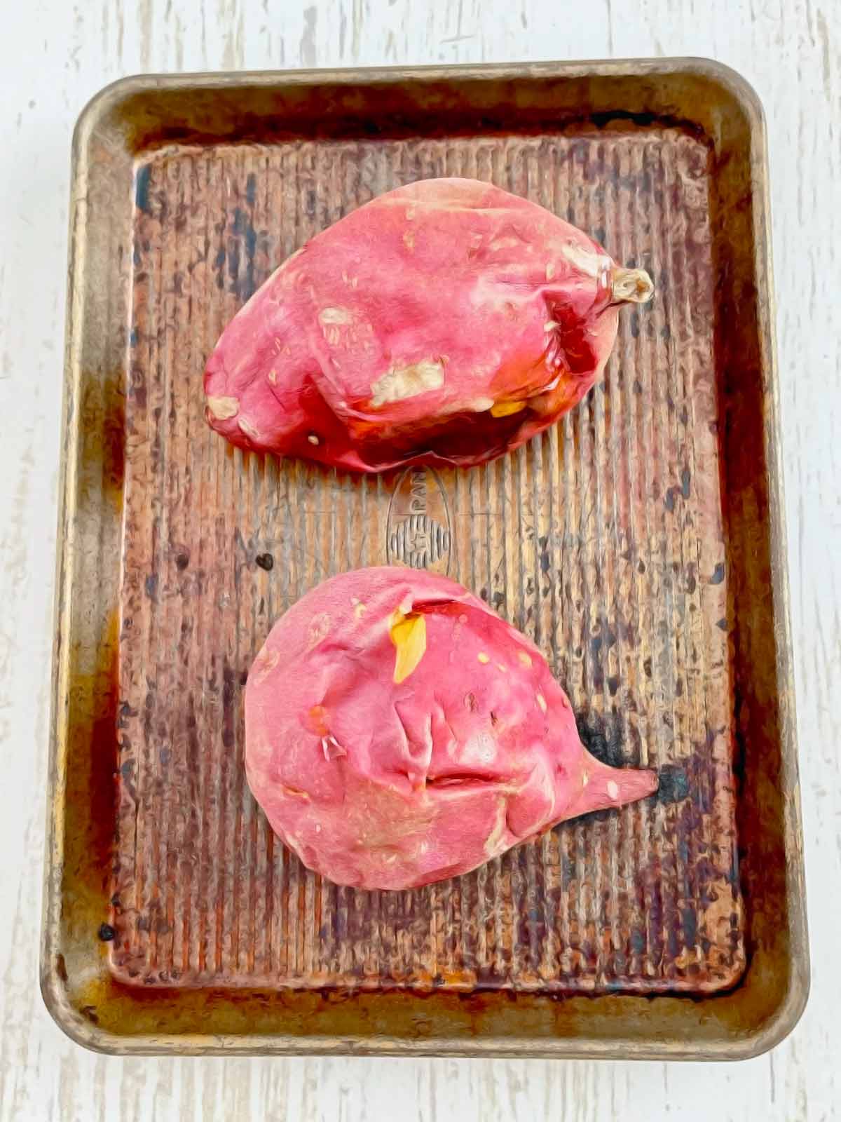 Fully cooked sweet potatoes with shrunken skin still on baking tray.