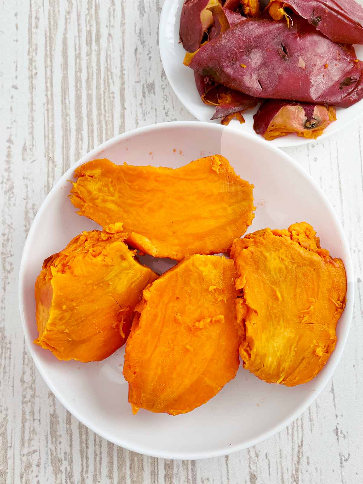 Bowl of peeled sweet potatoes alongside a plate with the peels.