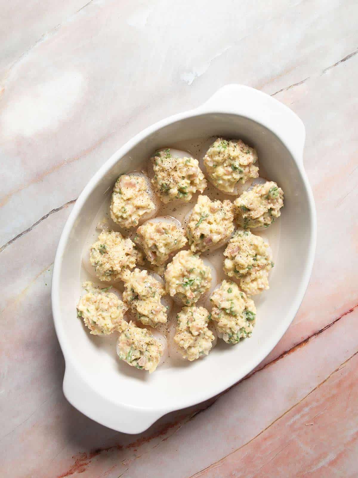 Scallops in the baking dish with topping on top on each one and wine poured in the bottom.