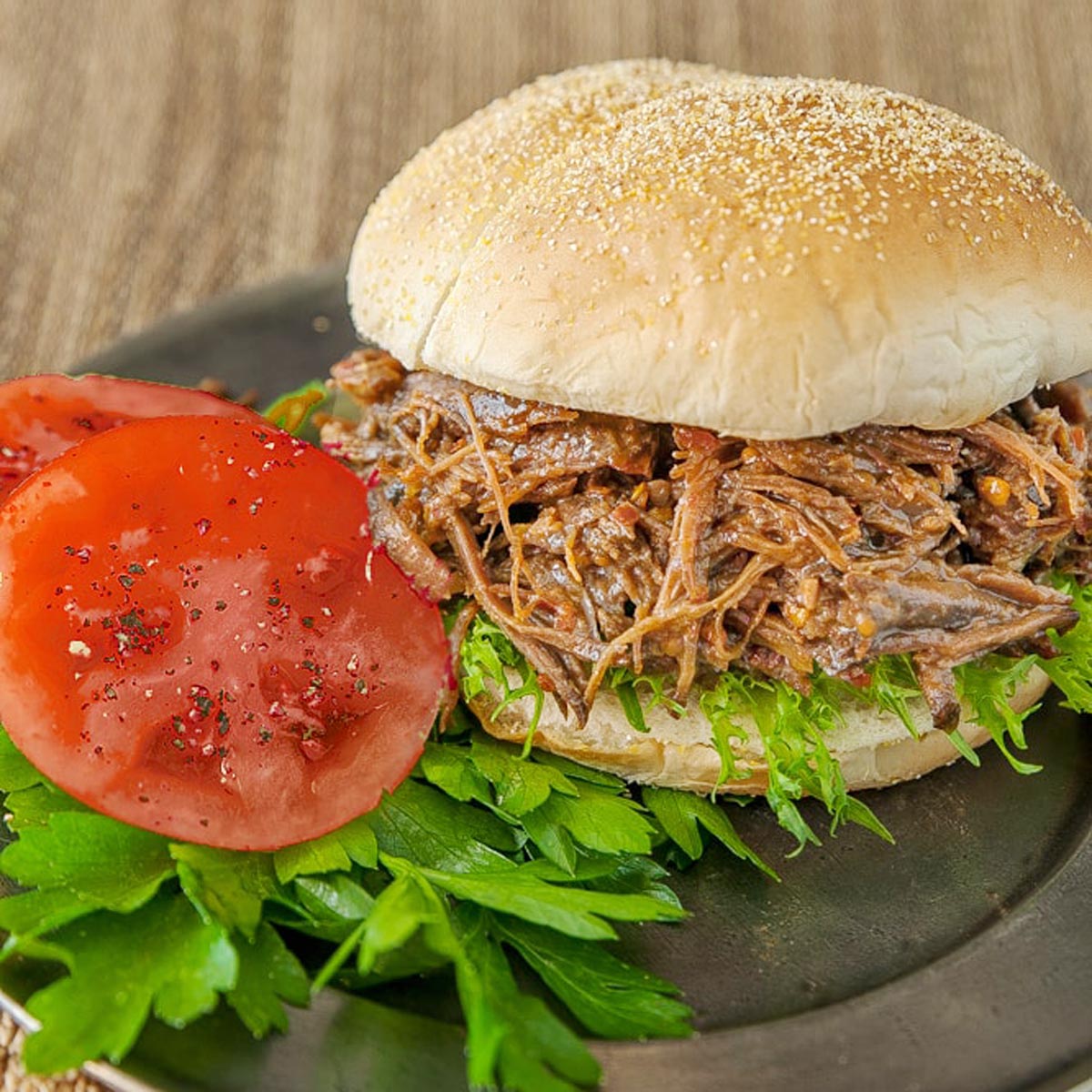 Sandwich with shredded beef on bun and tomatoes on the side.