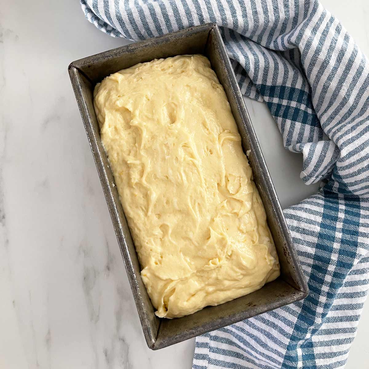 Batter in the loaf pan with blue dishtowel.