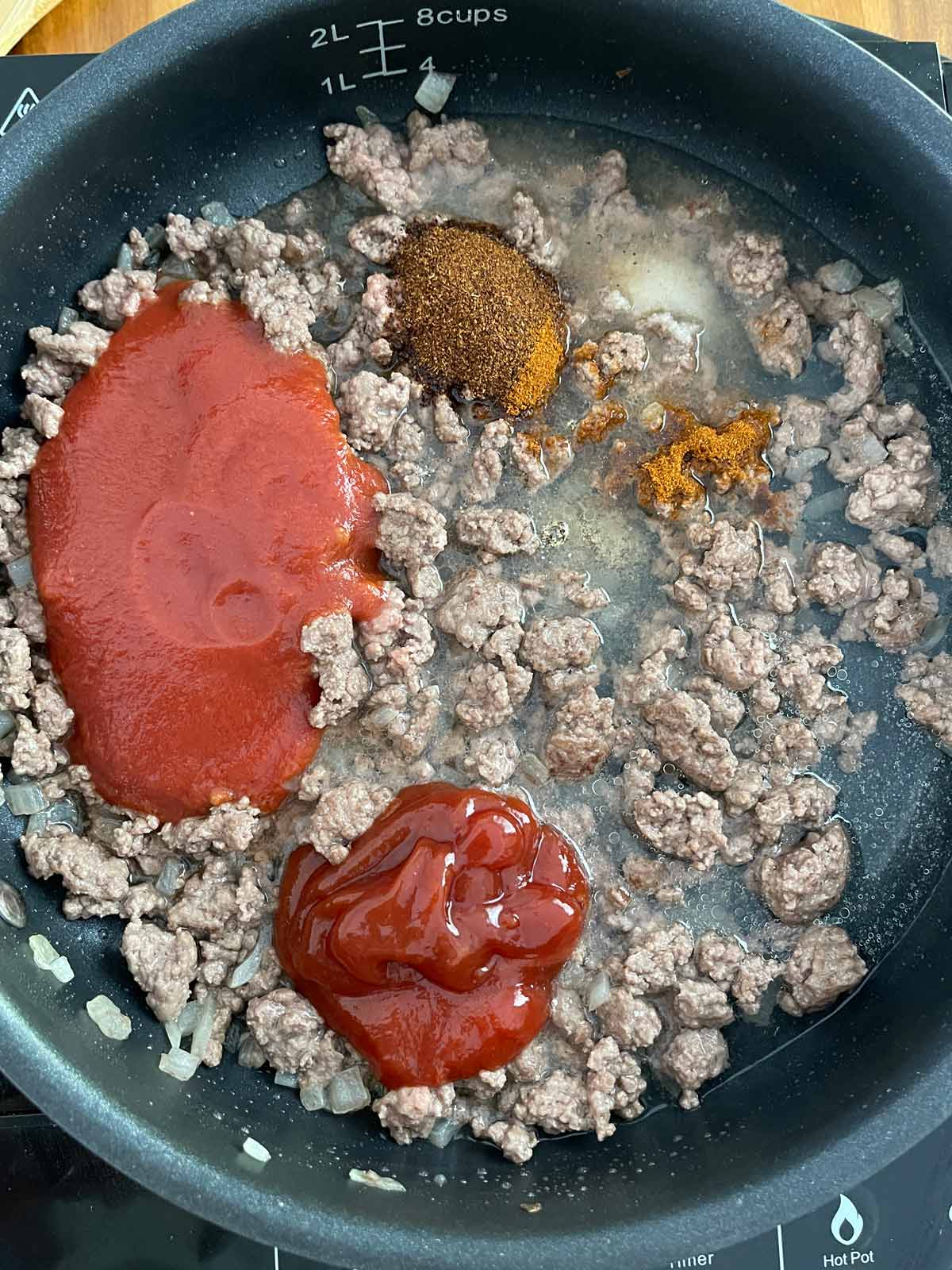 Skillet with browned beef, spices, tomato sauce, ketchup, and water added.