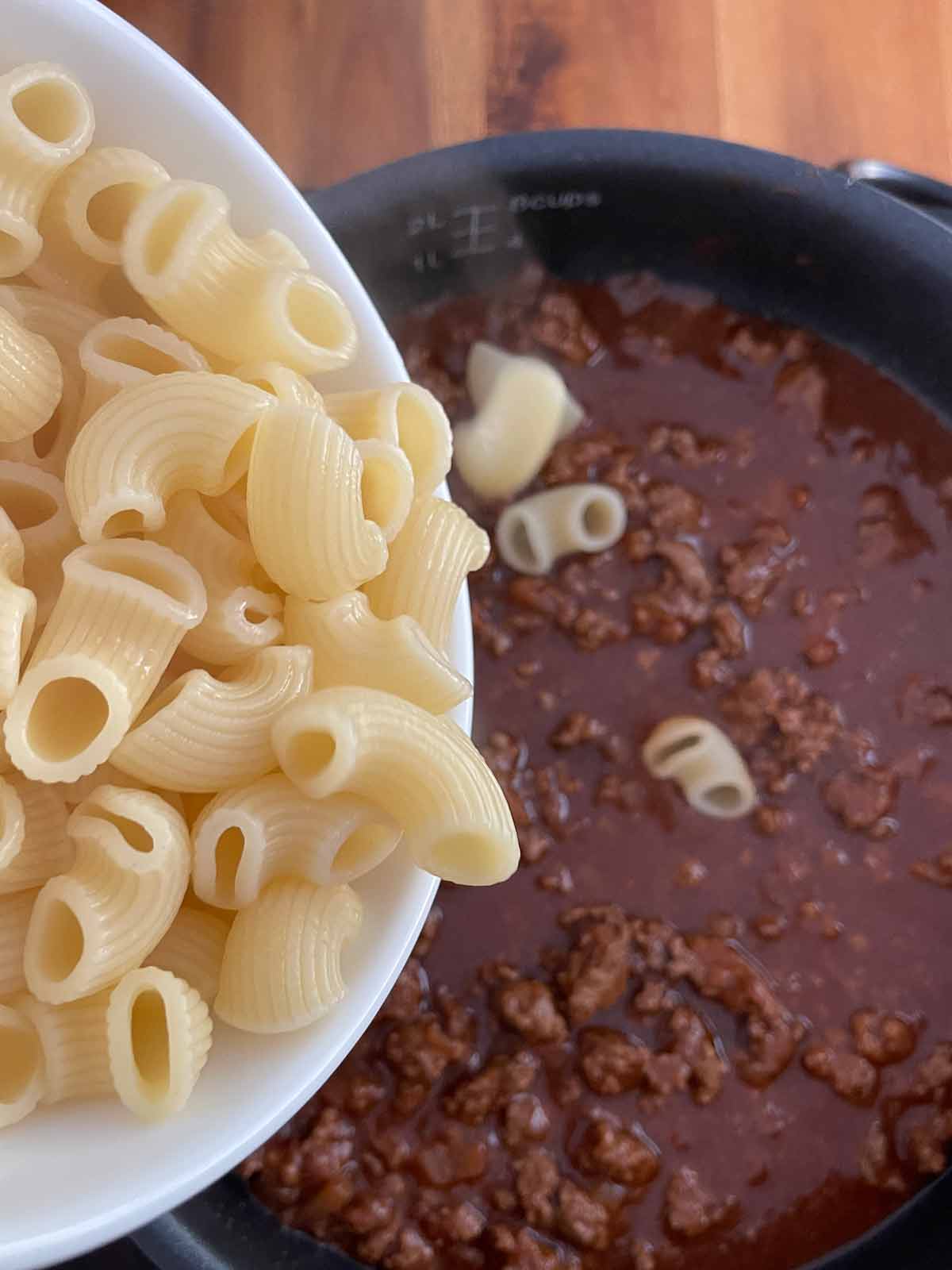 Cooked pasta being added to the chili mixture in the skillet.