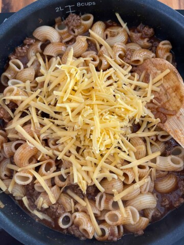 Adding cheese to the macaroni chili mixture in the skillet.