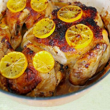 Golden brown chicken cooked under a brick with sliced Meyer lemons.