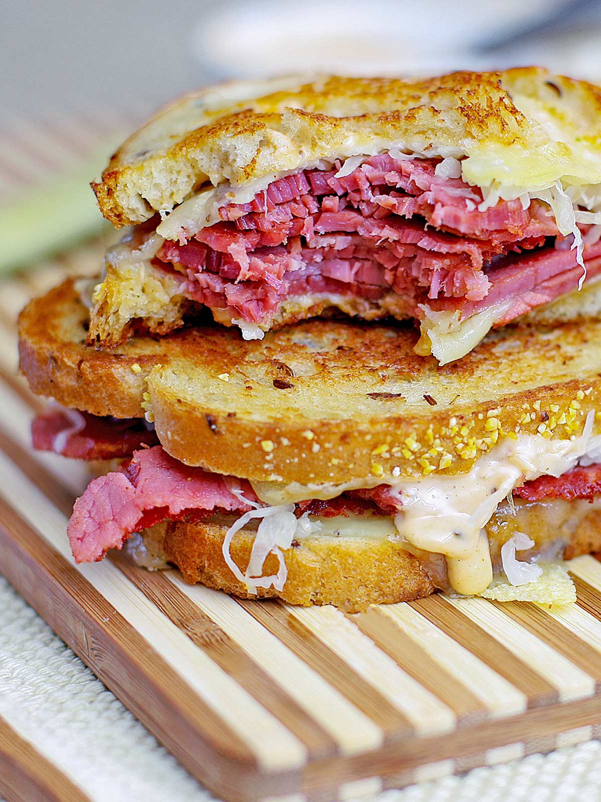 Corned beef sandwich cut in half with sauce and cheese oozing out.