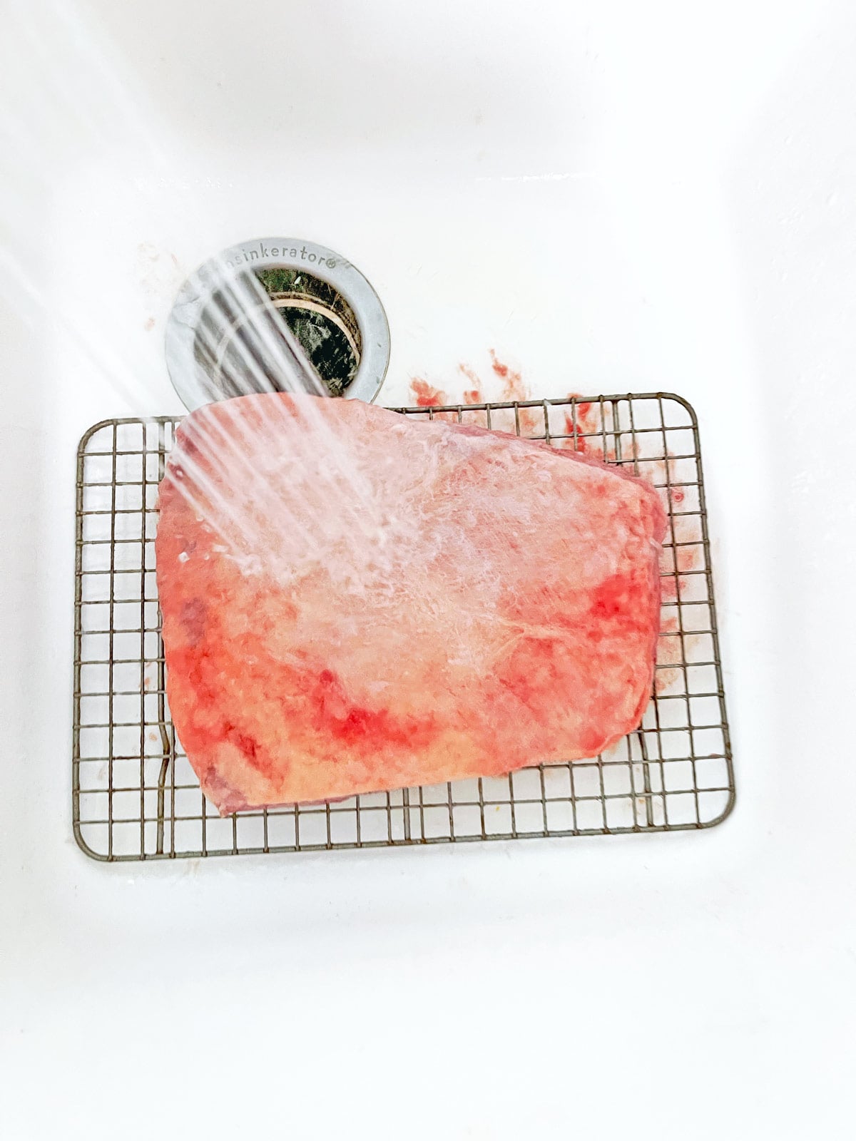 Water spraying down on corned beef in sink.