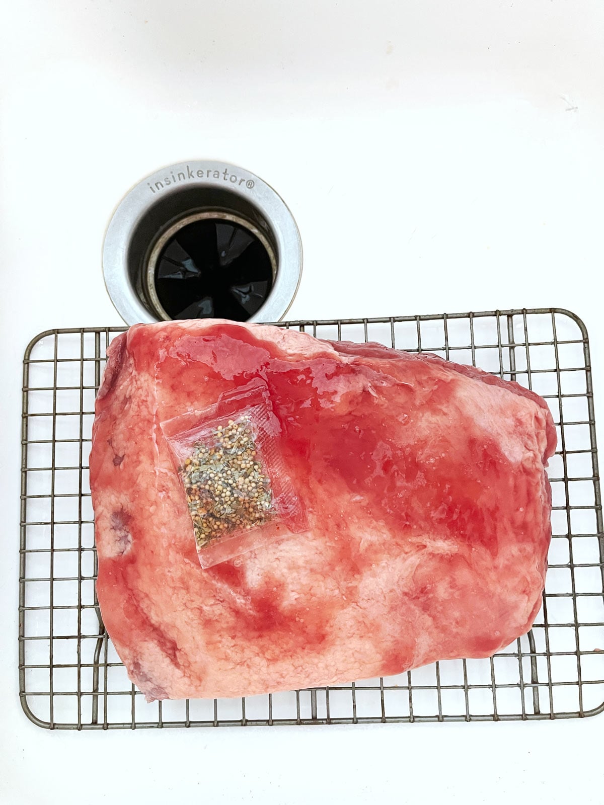 Wire rack with corned beef and spice packet in sink.