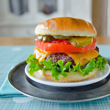Hamburger with pickles, tomato, burger patty with melted cheese,and lettuce on a bun.