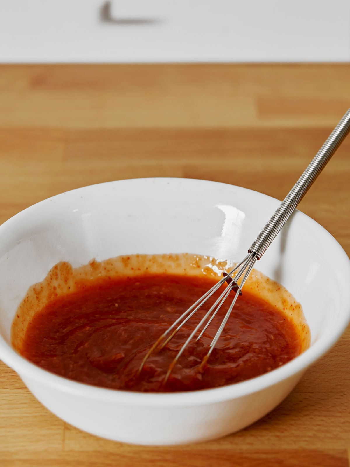 A bowl of cocktail sauce with a whisk in it used for making roasted shrimp cocktail.