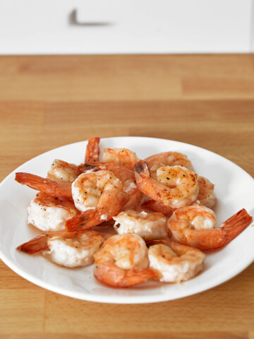 A plate of roasted shrimp on a wooden table.