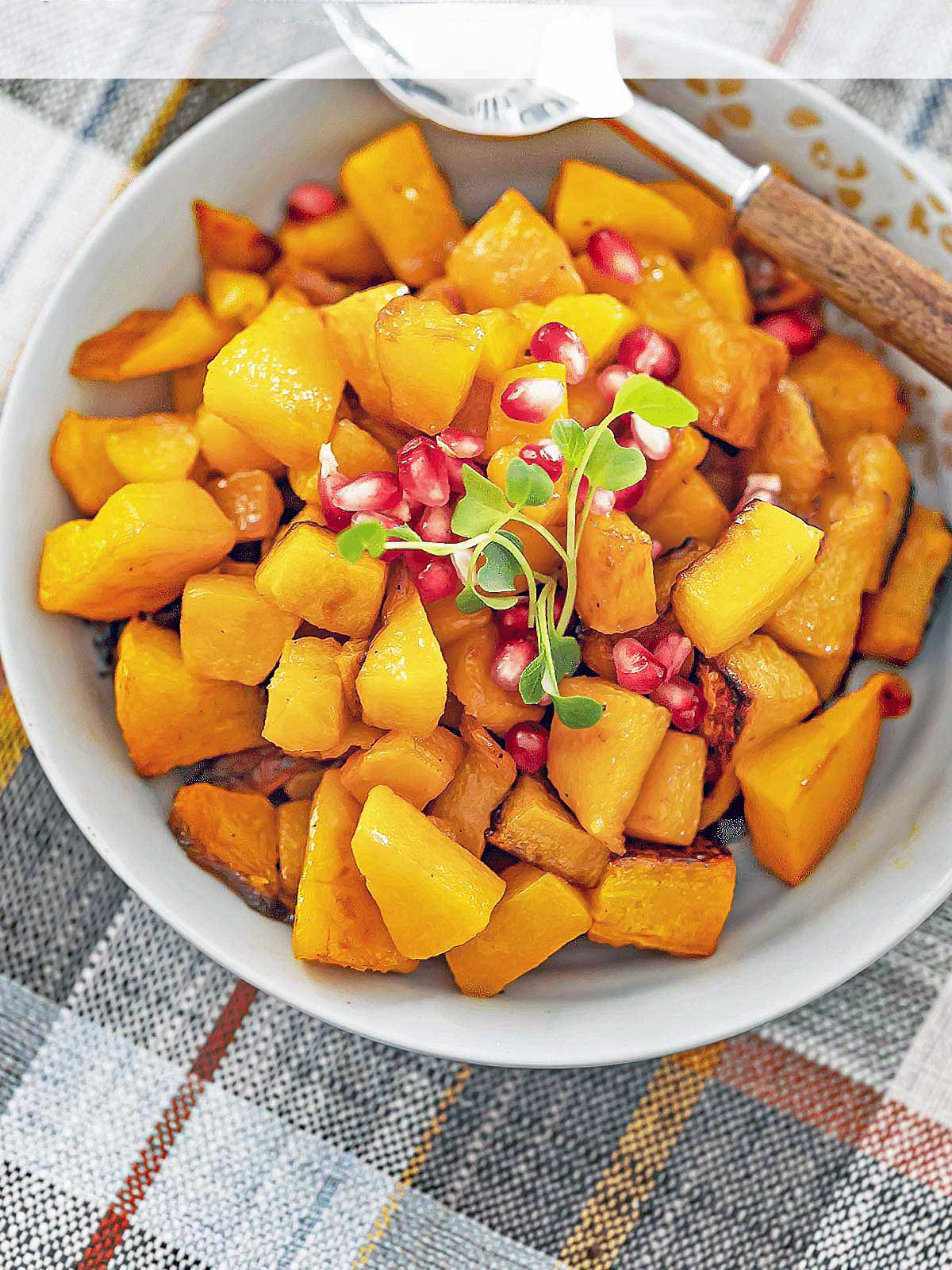 Bowl of beautifully caramelized butternut squash with pomegranate seeds on top.