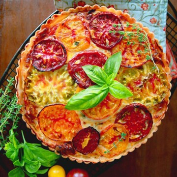 Baked round tart with tomatoes, basil, and fresh thyme garnish.