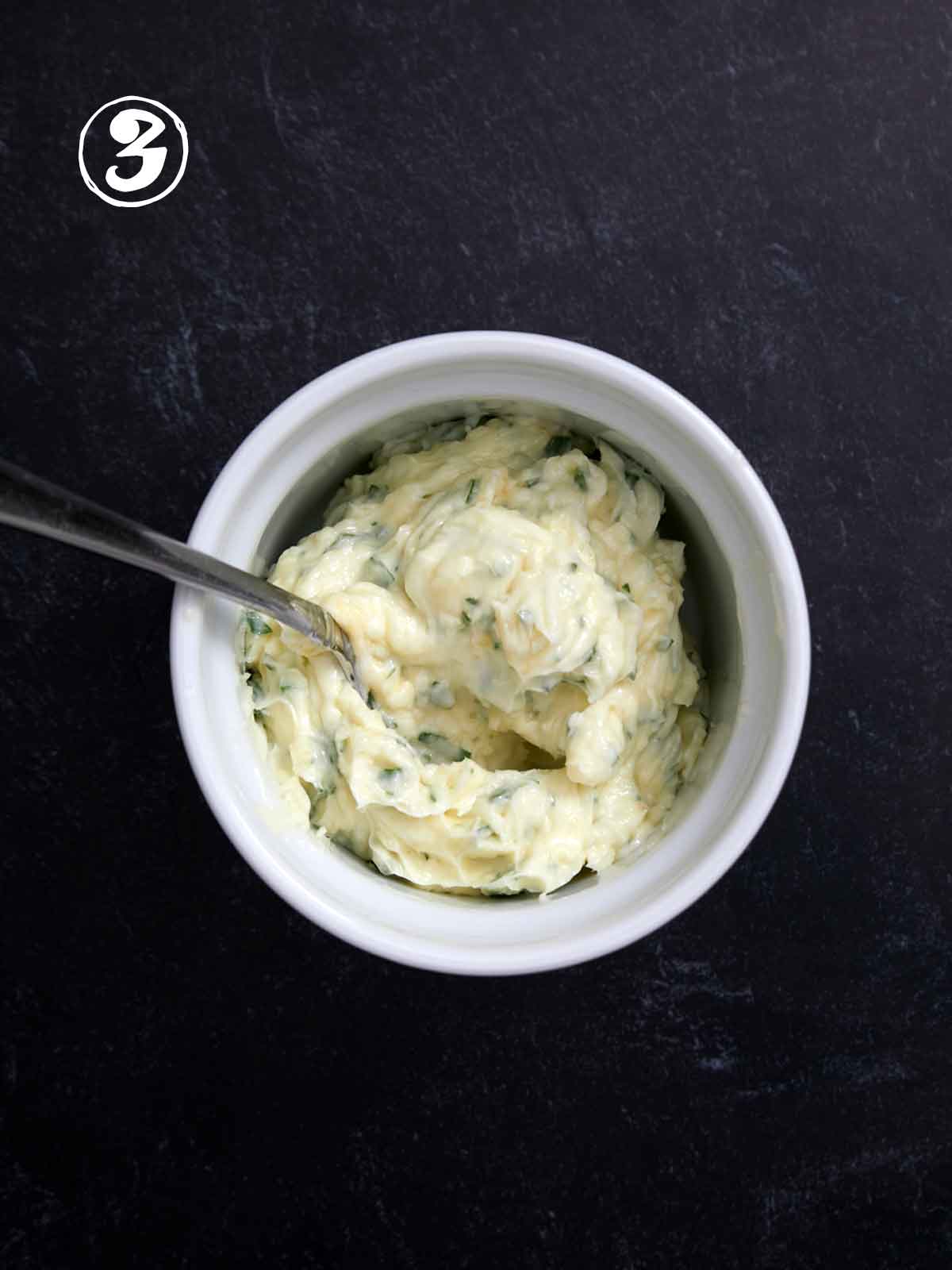 A bowl of garlic butter with a spoon in it.
