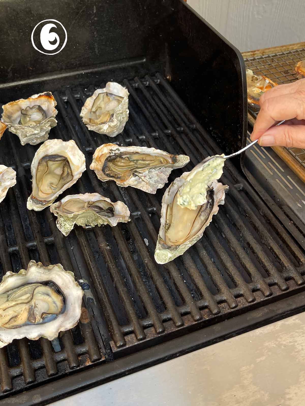 A person is grilling oysters adding butter.