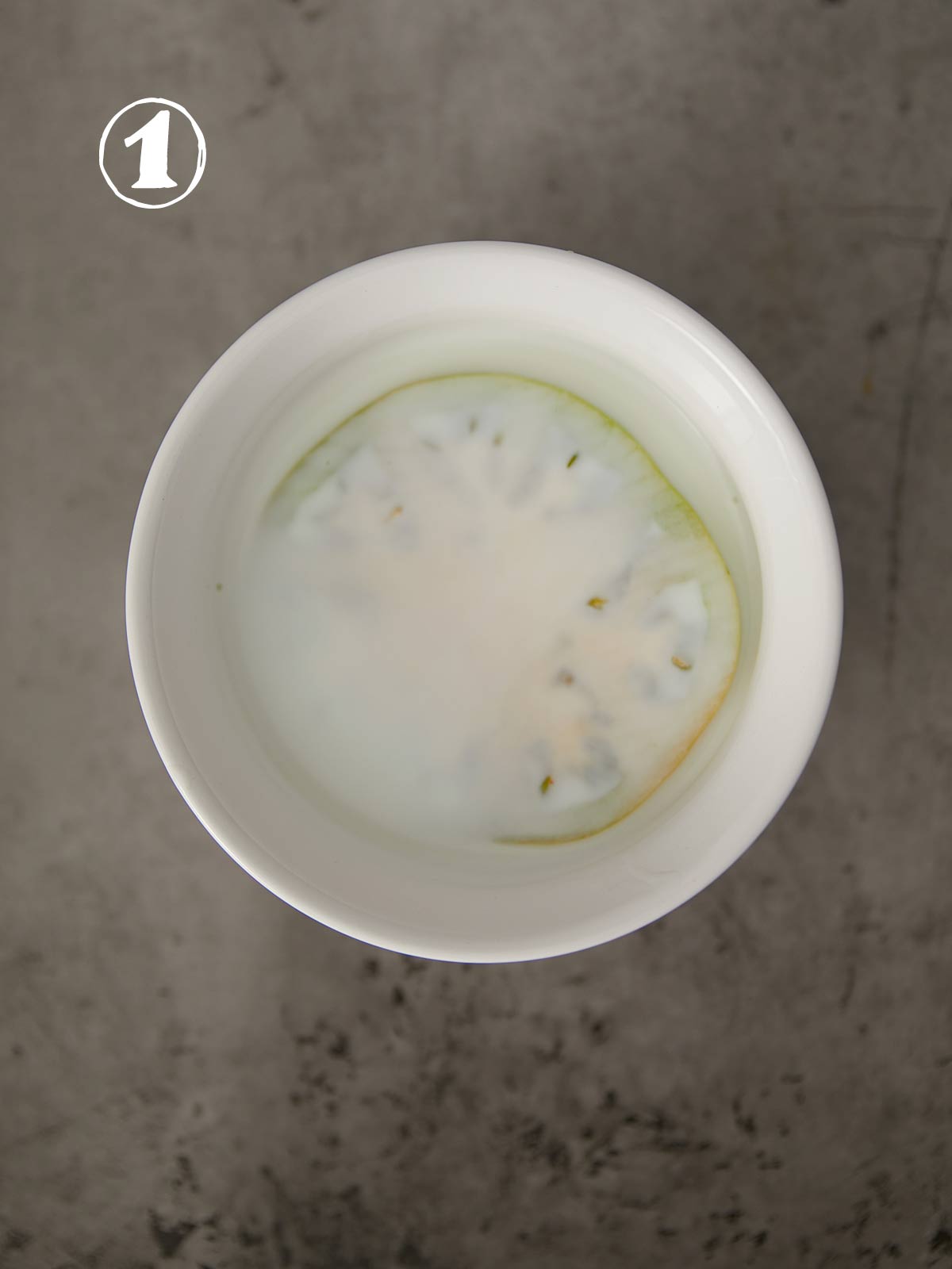 A bowl of water with a slice of cucumber fried in it.
