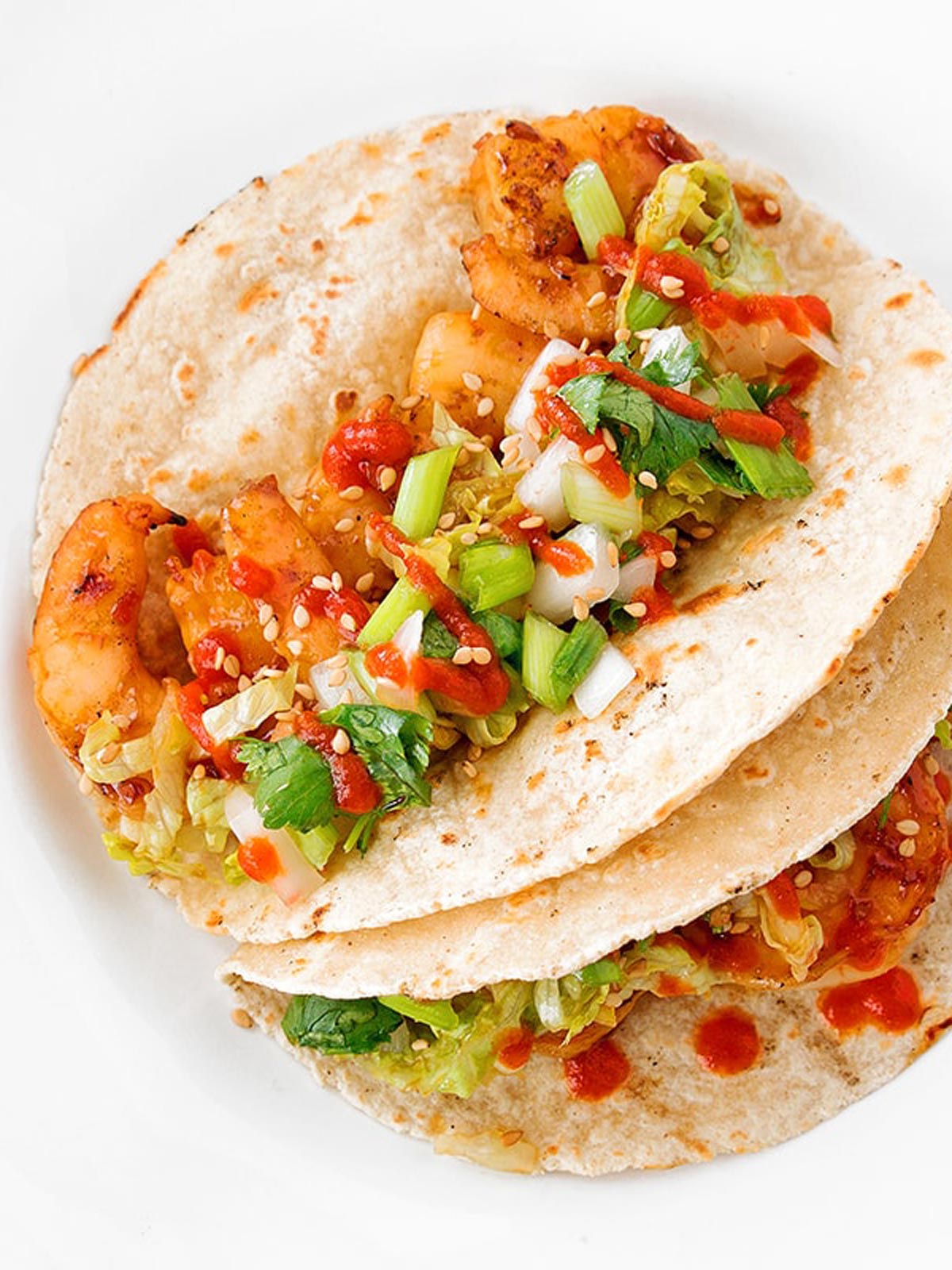 Picture of two shrimp tacos with green onion and sauce.