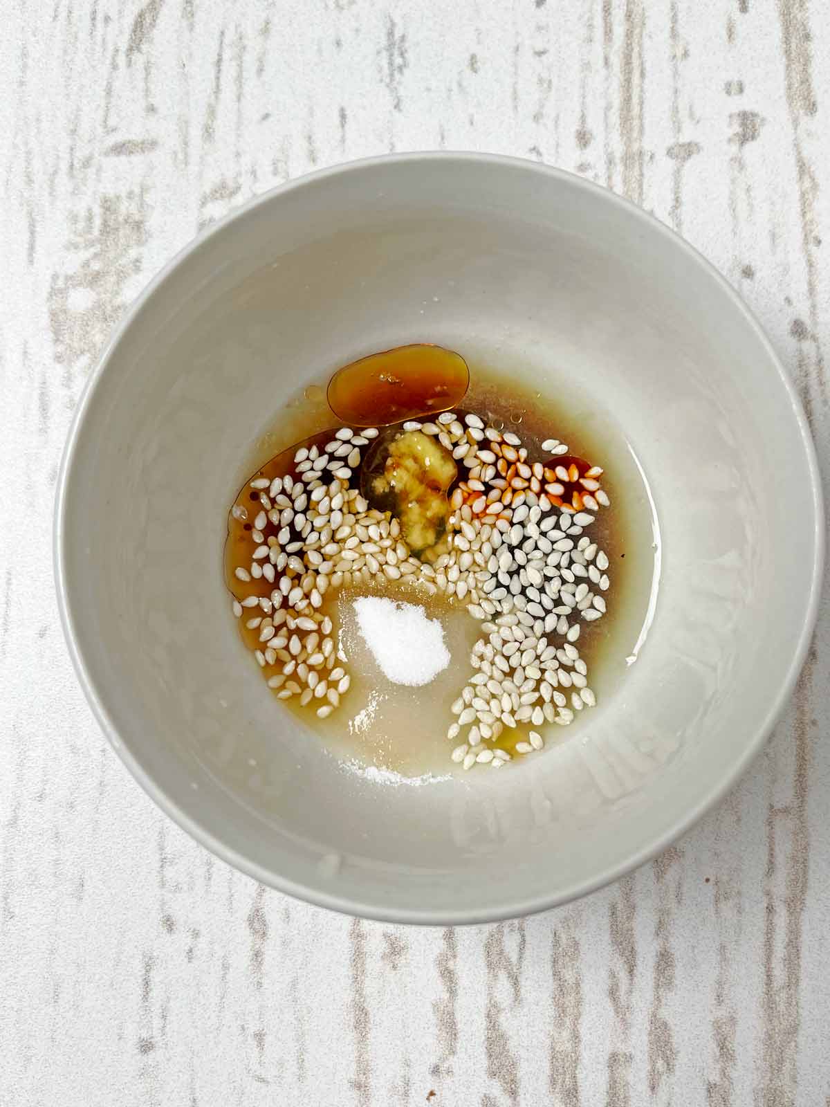 Small bowl of sesame seeds, sugar, lime juice, chili sauce, soy sauce, and sesame oil.
