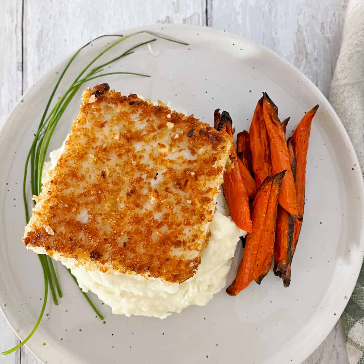 Cooked, golden brown halibut on a plate with mashed potatoes and roasted carrots.