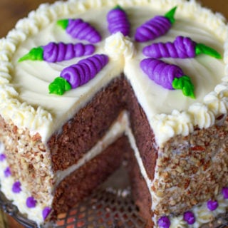 A purple carrot cake with purple piped carrot s on top.