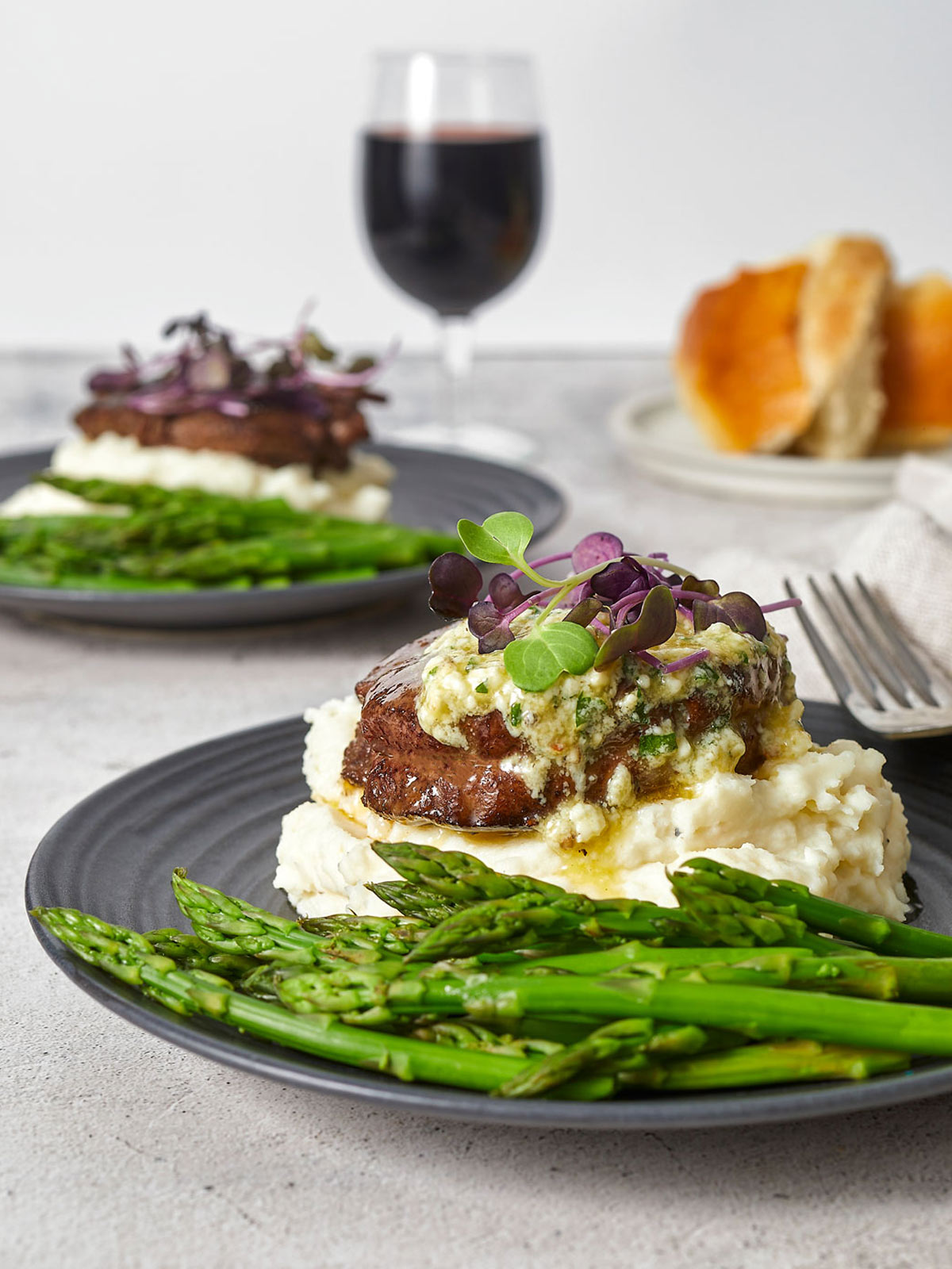 Plate with mashed potatoes, asparagus, and filet Mignon, topped with melting butter.