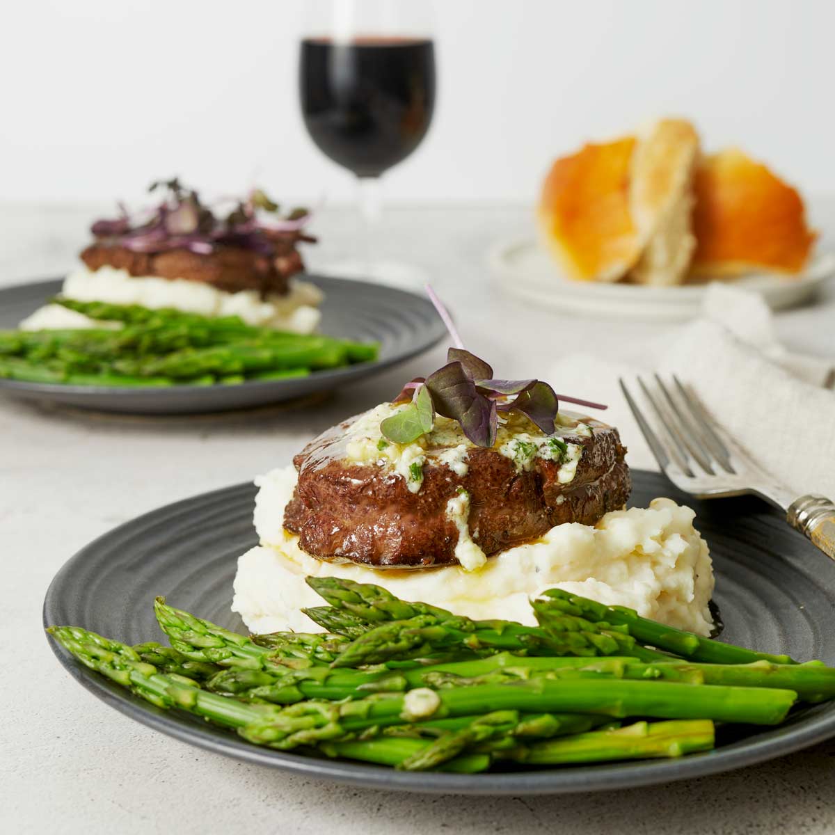 Plate with steak with melted butter on top dripping down sides of steak and onto mashed potatoes.