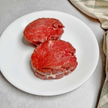 Two Filet Mignon steaks tied in a circle with butcher's twine on a plate. 