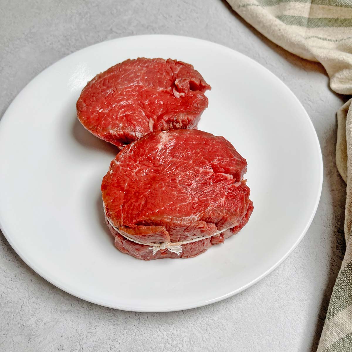Two Filet Mignon steaks tied in a circle with butcher's twine on a plate.