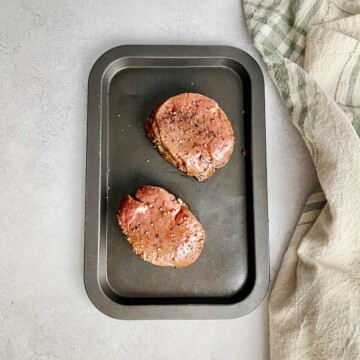 Small baking tray with 2 marinated steaks.
