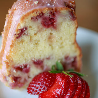 Slice of strawberry cake on a plate with sliced strawberries.
