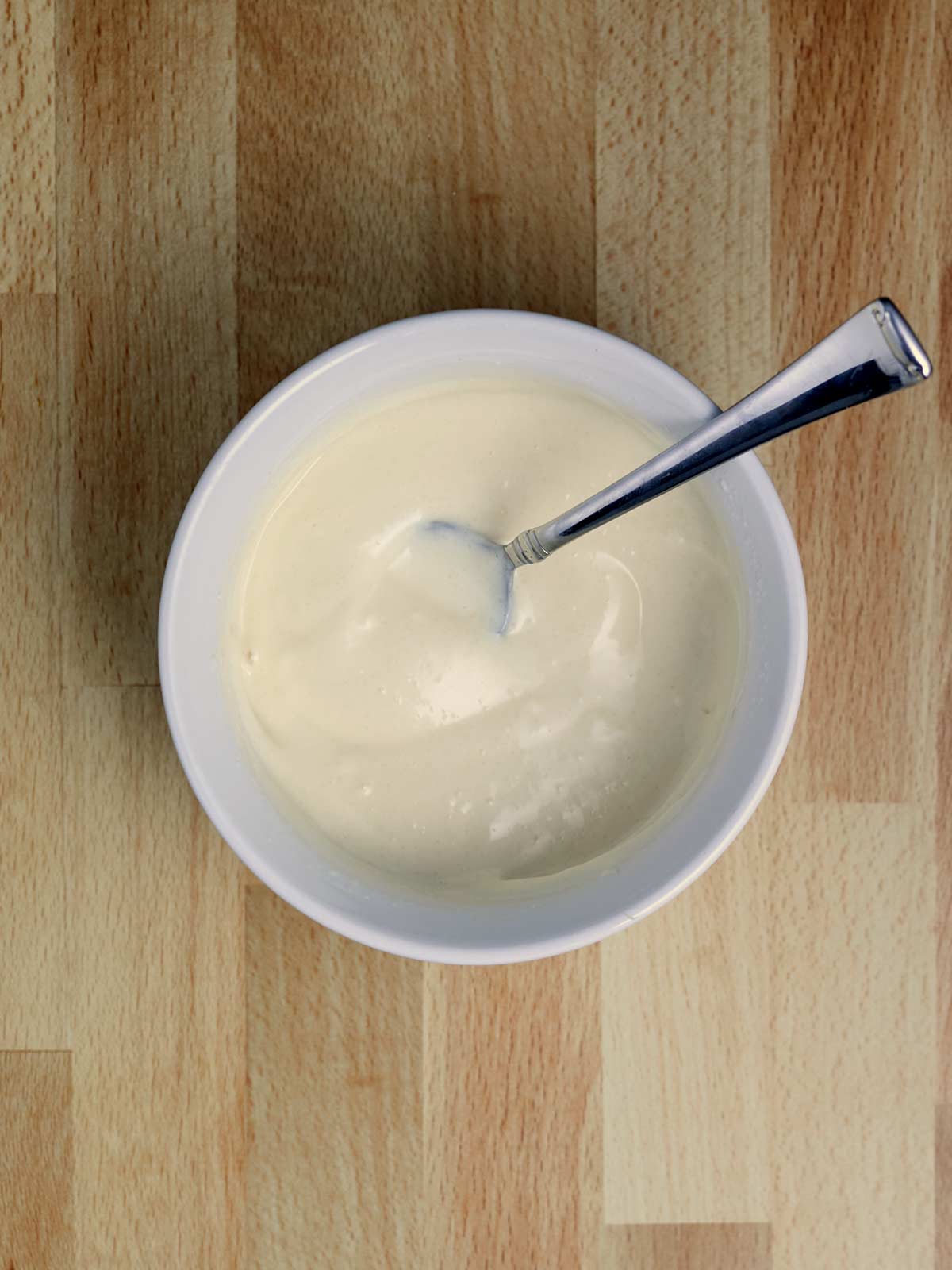A bowl of dressing with a spoon on a wooden table.