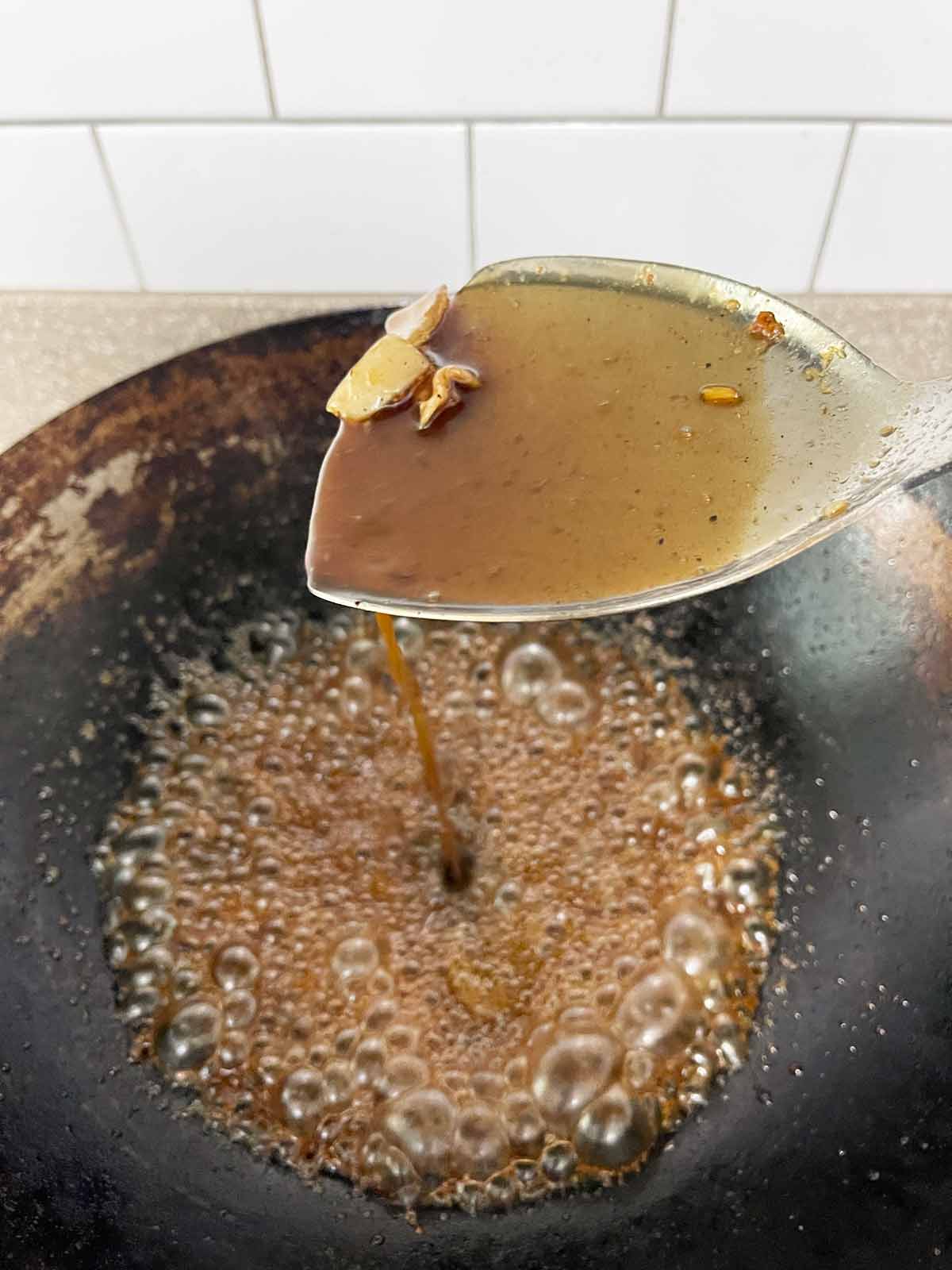 Ladle stirring the sauce as it thickens in the hot wok.