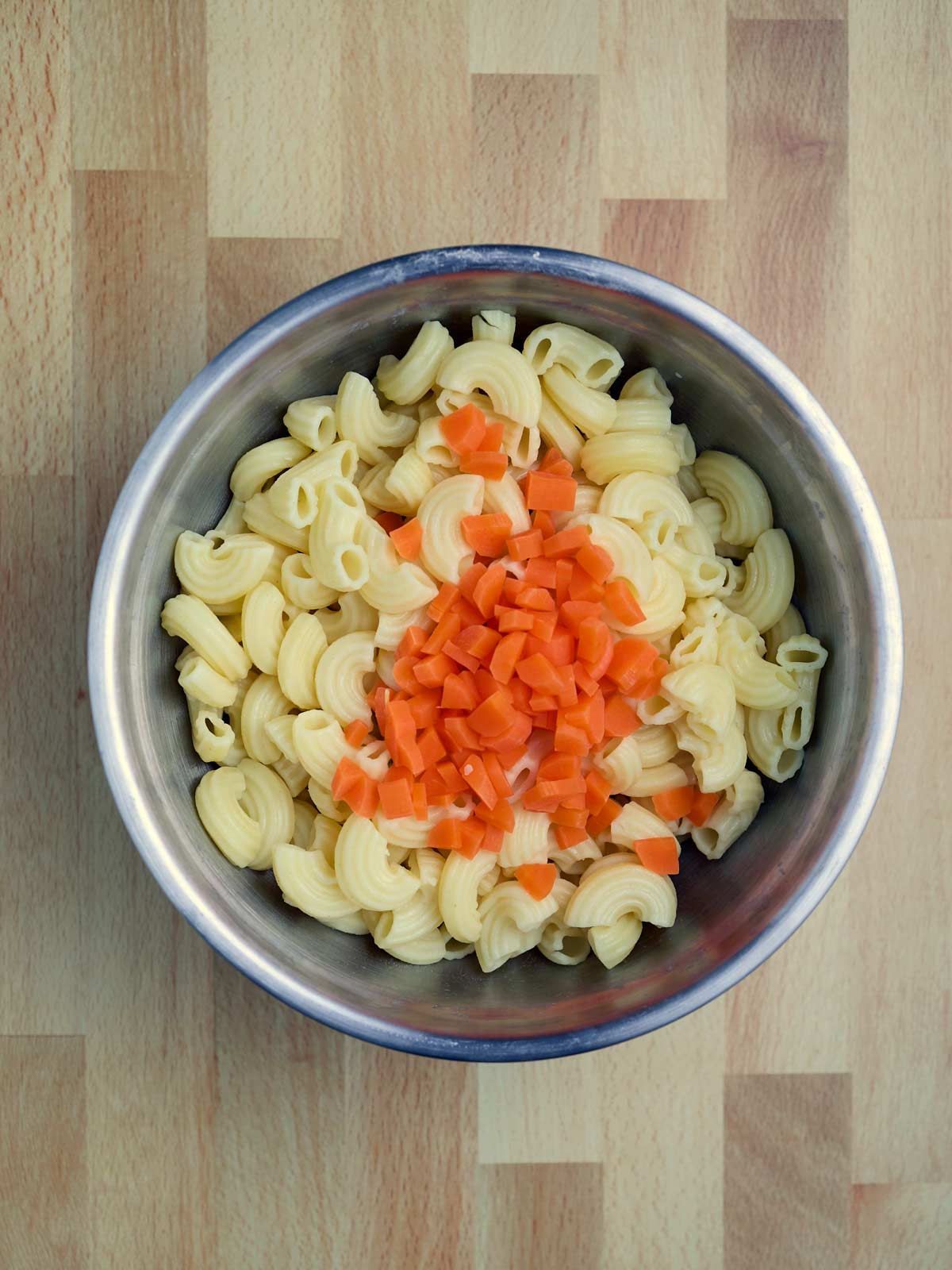 Hawaiian Style Macaroni Salad with pasta and carrots in a bowl on a wooden table.