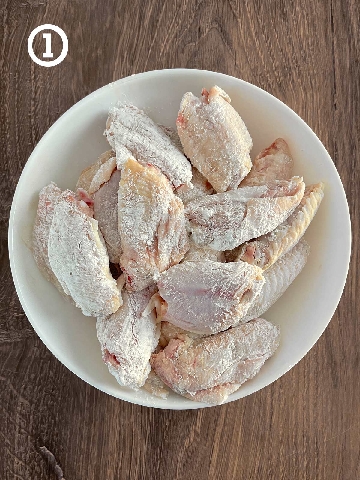 Grandmother's Chinese Chicken Wings tossed in cornstarch and baking soda in a white bowl on a wooden table.