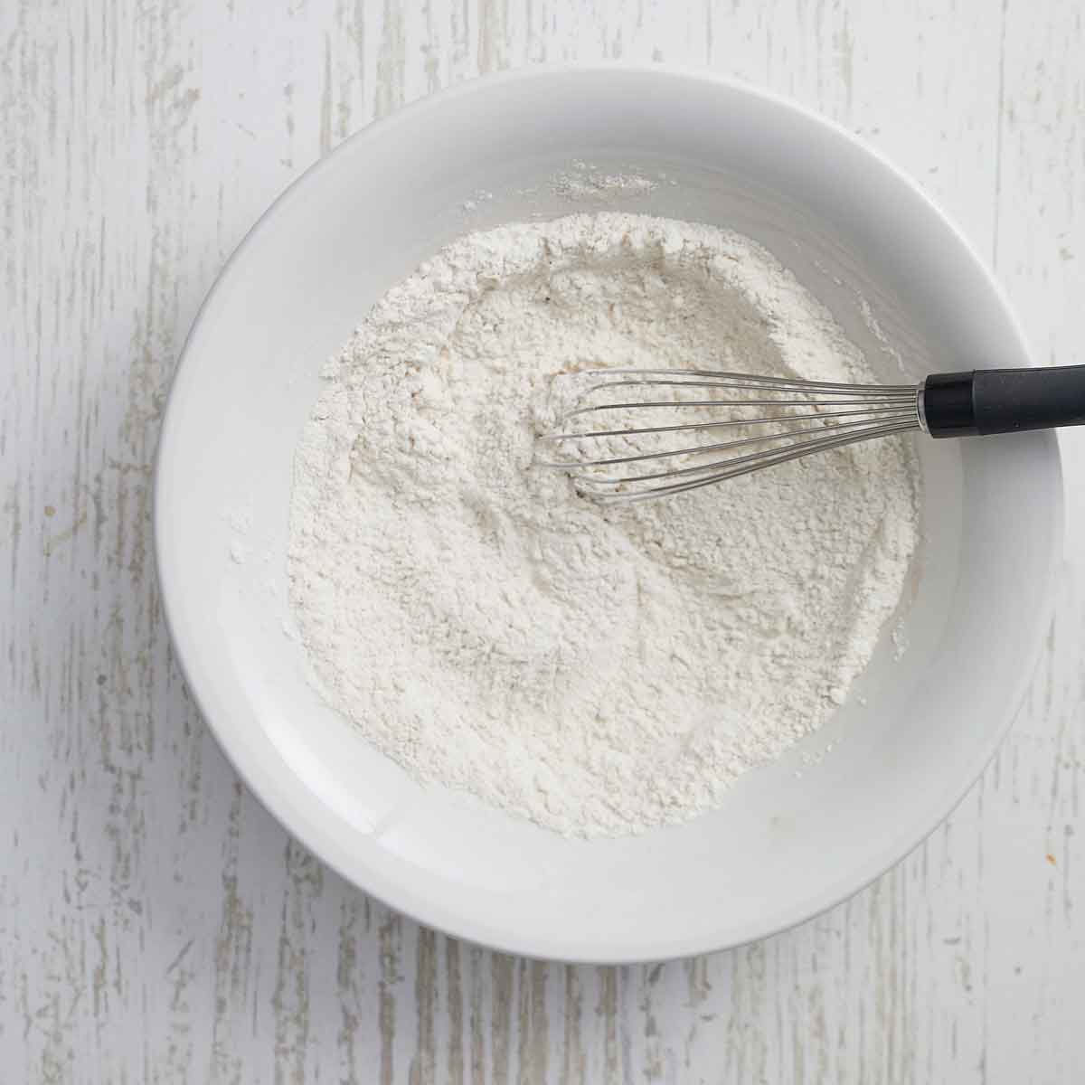 Flour and spices whisked with a whisk in bowl.