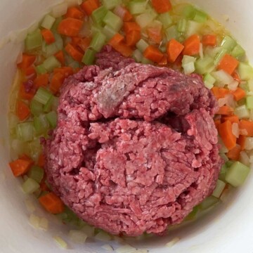 Image with pot of vegetables with raw ground beef added.