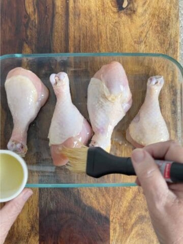 Chicken drumsticks being brushed with oil.