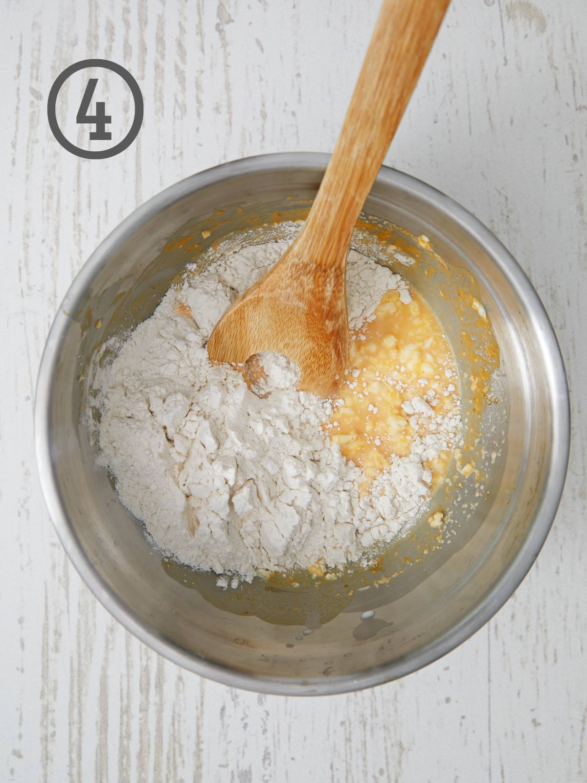 A wooden spoon is being used to mix flour and eggs in a bowl for a pumpkin dinner rolls recipe.