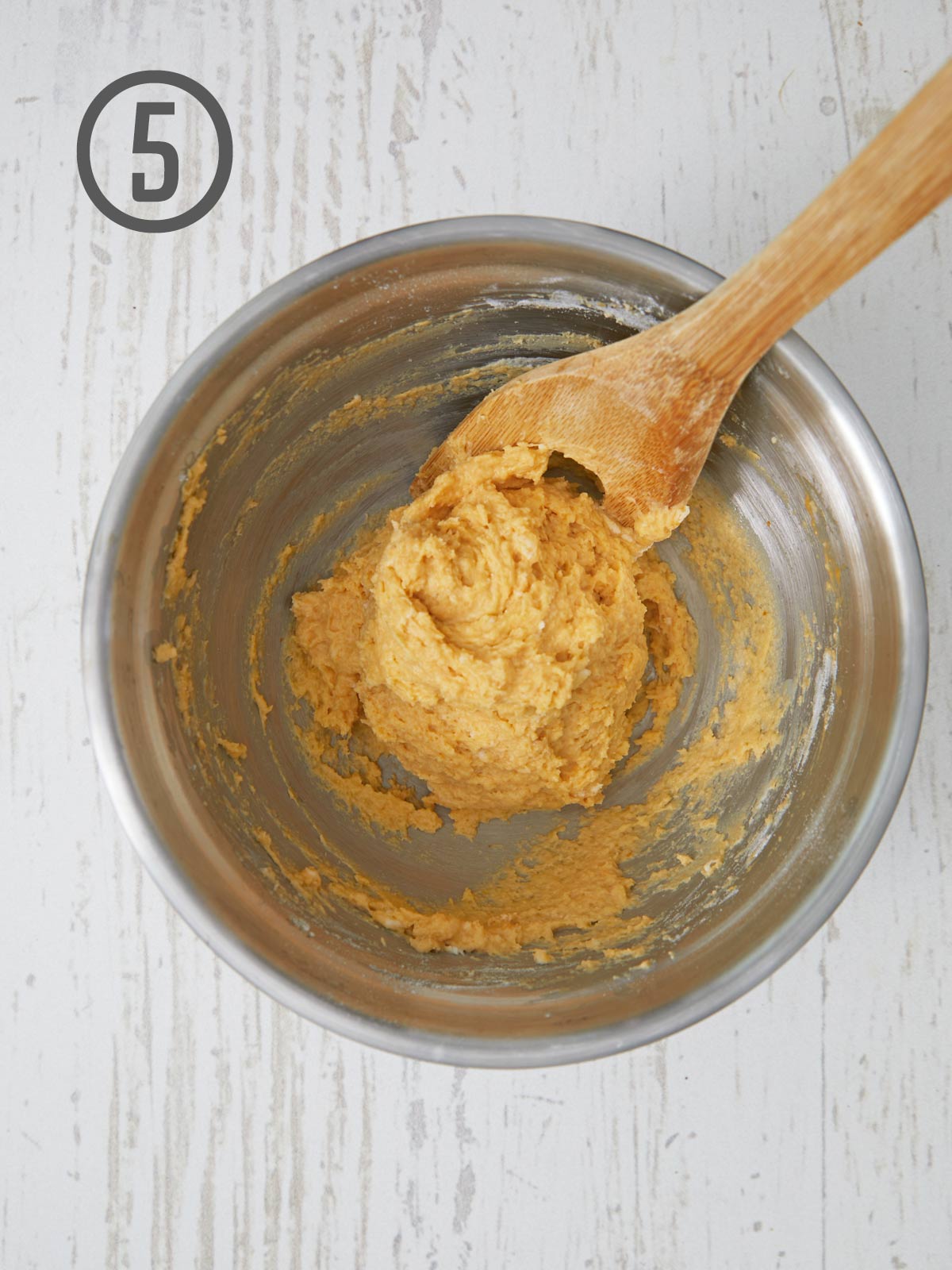 A wooden spoon is used to mix the ingredients in a pumpkin dinner rolls recipe.